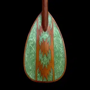 Close-up studio photography of the paddle for a wooden paddleboard by Little Bay Boards, showcasing rich natural wood textures and a deep forest green chevron art inlay over a solid black backdrop.